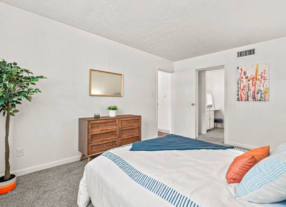 A bedroom with a bed, dresser, and a plant.