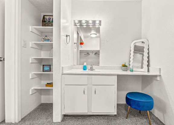 A white bathroom with a sink, mirror, and a blue stool.