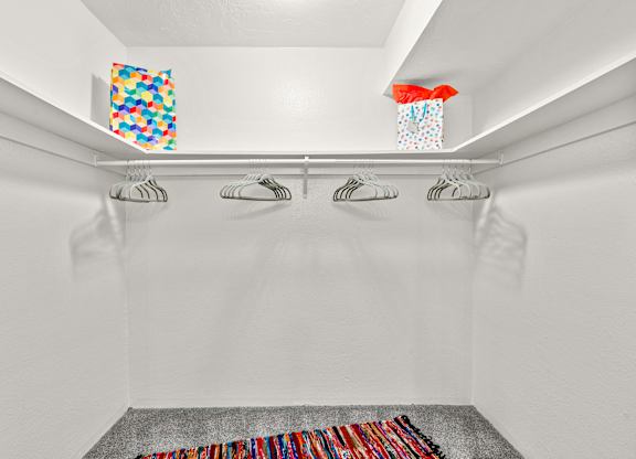 A white closet with a grey carpet and clothes hanging on the hangers.
