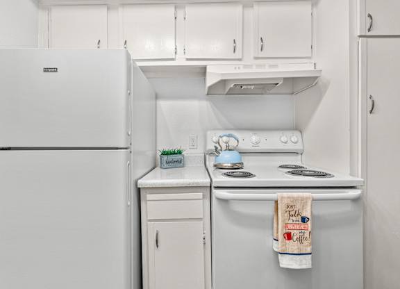 A white kitchen with a fridge, stove and cabinets.