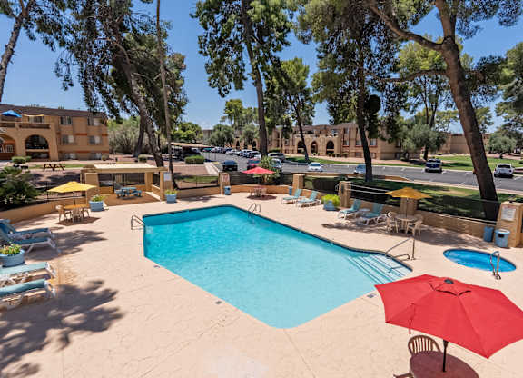 A pool surrounded by chairs and trees.