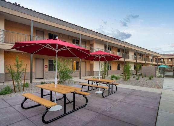 A patio with red umbrellas and benches in front of a building.