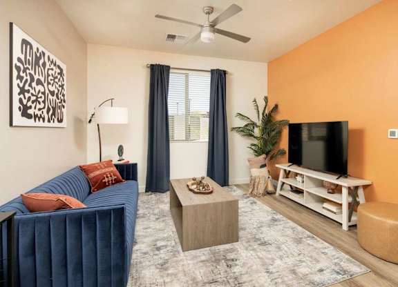 A living room with a blue couch, a television, and a ceiling fan.