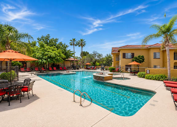 A large swimming pool surrounded by red lounge chairs and umbrellas.