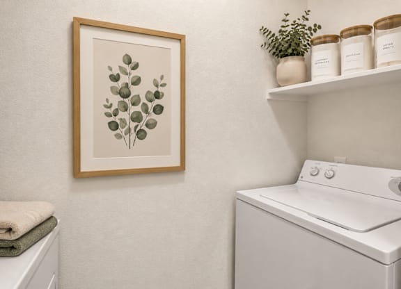 A picture of a plant is hanging on a wall above a washing machine.