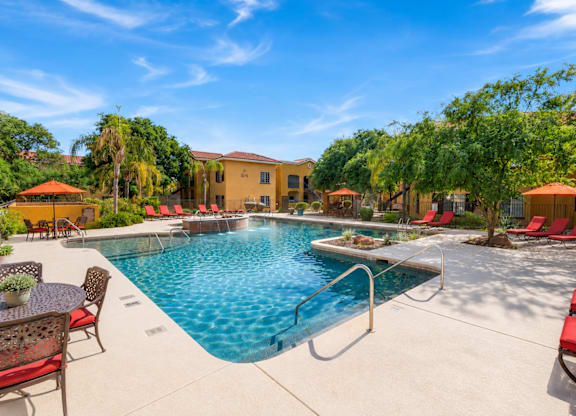 A pool surrounded by red chairs and trees.