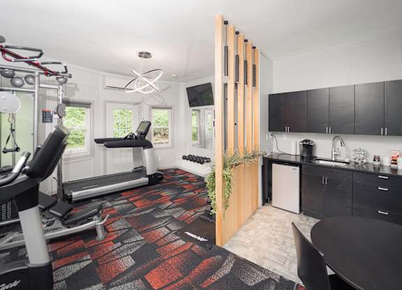 a gym with a reformer exercise machine and a kitchen with black cabinets at Woodbury Knoll, Woodbury, CT 06798