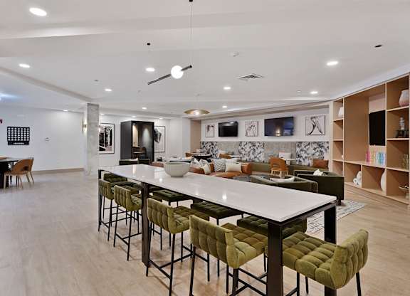 A modern kitchen with a long white island and green barstools.