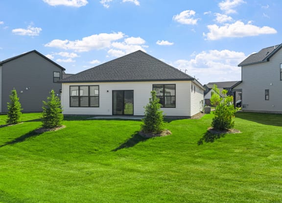 the front of a house with a green lawn and some small trees