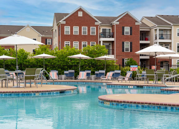 a swimming pool with lounge chairs and umbrellas in front of a brick building