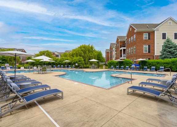 a swimming pool with chaise lounge chairs and umbrellas in front of a brick building