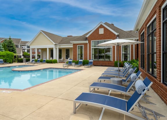 a swimming pool with chaise lounge chairs and umbrellas in front of a brick building
