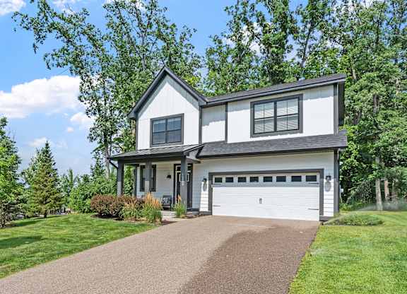 A two-story house with a garage is surrounded by greenery.