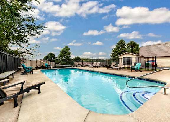 A large outdoor swimming pool surrounded by a fence and lounge chairs.