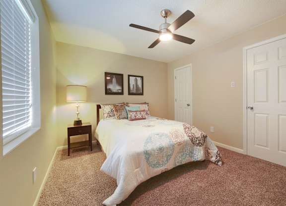 A bedroom with a bed, a ceiling fan, and two pictures on the wall.