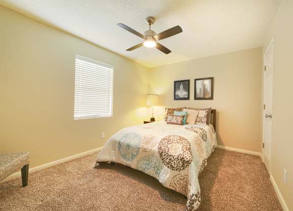 A bedroom with a bed, a bench, and a ceiling fan.