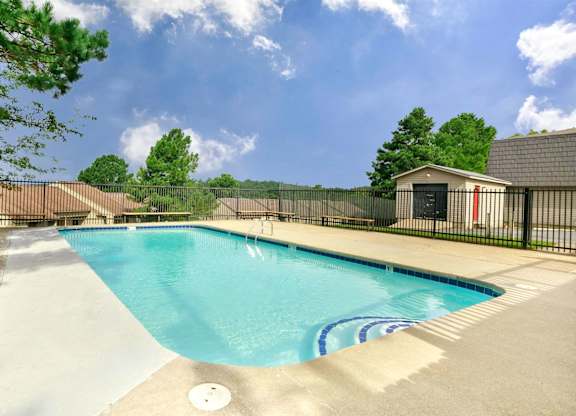A small pool with a black fence and a small building in the background.