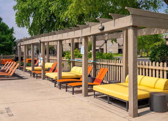 a row of orange and yellow lounge chairs under a wooden pergola