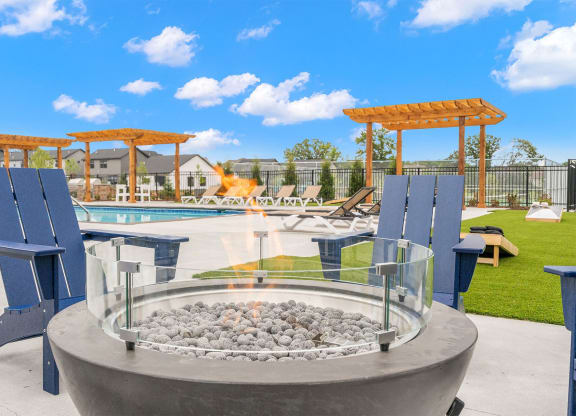 a fire pit with blue chairs around it near a pool