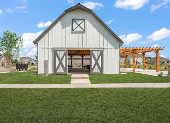 A white barn-like building with a wooden roof and a green lawn in front.