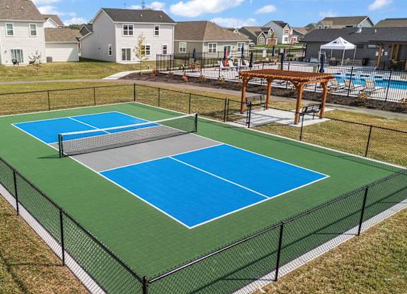 A tennis court with a green and blue surface surrounded by a black fence.