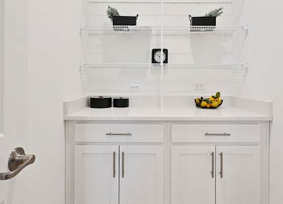 A kitchen with white cabinets and a white countertop with a bowl of fruit on it.