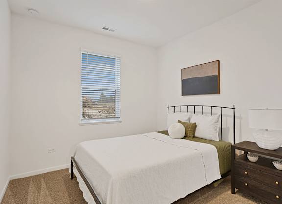 A bedroom with a bed, nightstand, and a window with blinds.