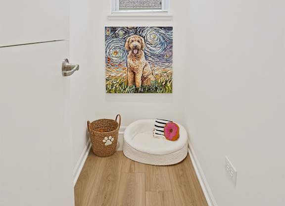 A dog painting hangs on the wall above a dog bed.