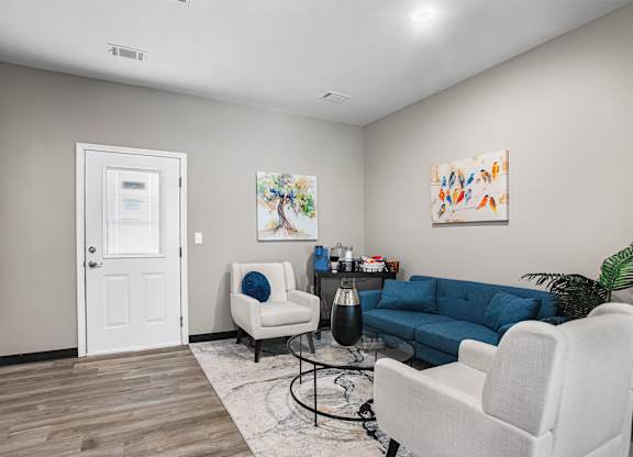 A living room with a white chair, a blue sofa, and a painting on the wall.