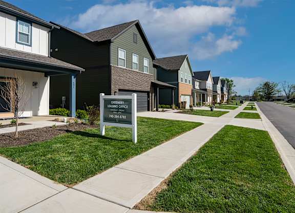 A sign in front of houses that says "The Grove" with a phone number.
