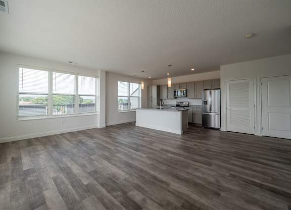 A spacious room with wooden flooring and a kitchen area in the background.