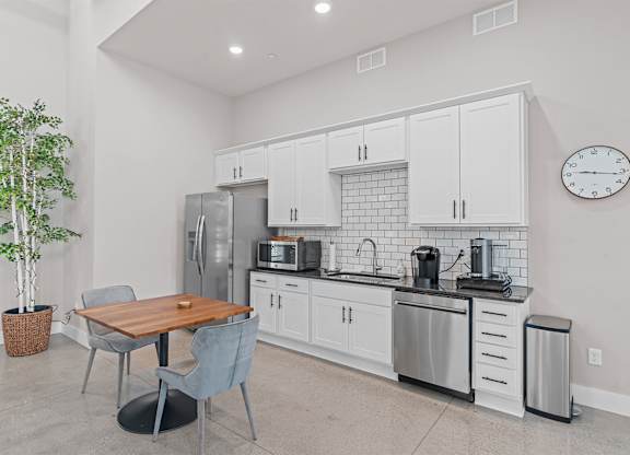A kitchen with a table and chairs in the foreground and a refrigerator, microwave, and oven in the background.