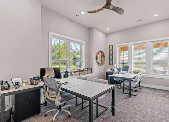 A modern office with a white desk and chairs, a phone, and a fan.