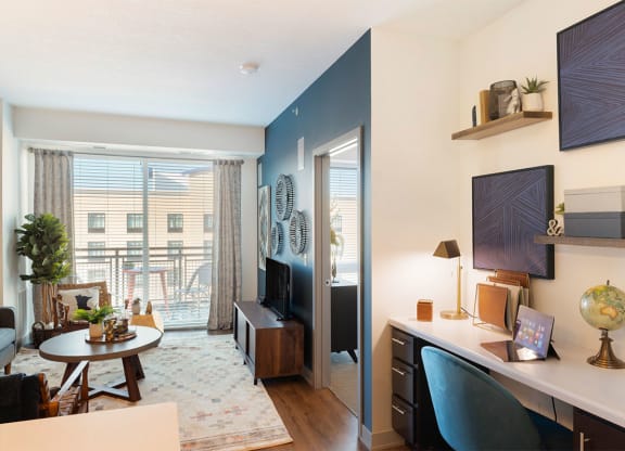 a living room with a desk and a door to a balcony