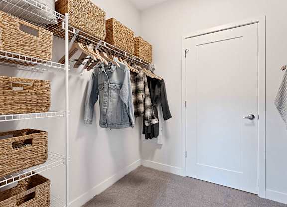 A white closet with clothes hanging and baskets on shelves.