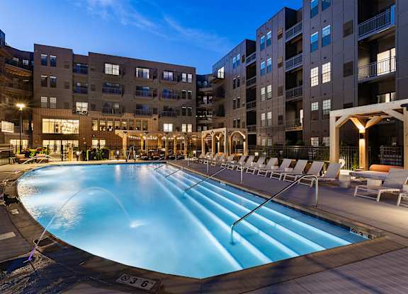 A large outdoor swimming pool surrounded by lounge chairs and buildings.