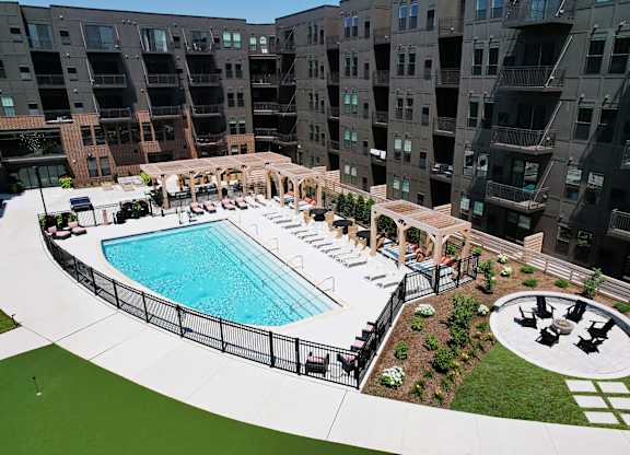 A large outdoor pool surrounded by a black fence and a small patio area with a table and chairs.