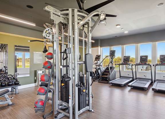 A gym with a variety of equipment including treadmills, weights, and a ceiling fan.