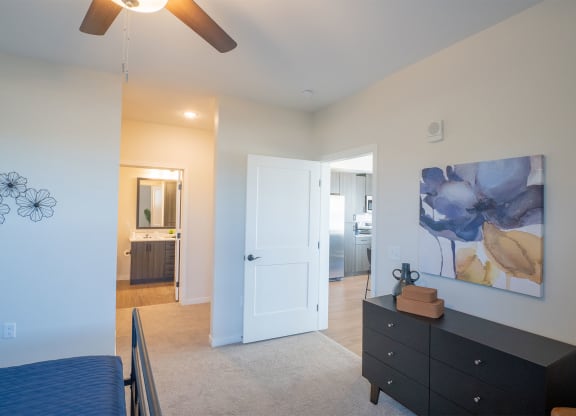a bedroom with a bed and a dresser and a hallway to a bathroom