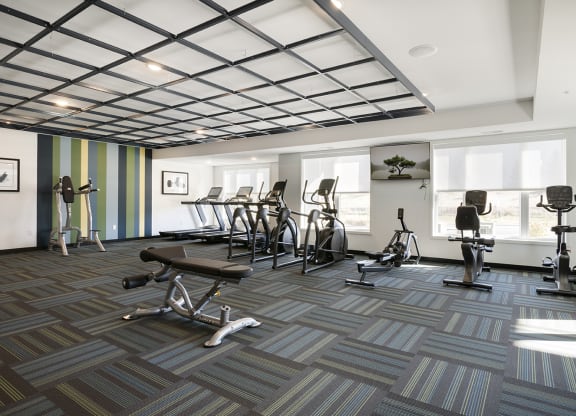 a spacious fitness room with exercise machines and windows