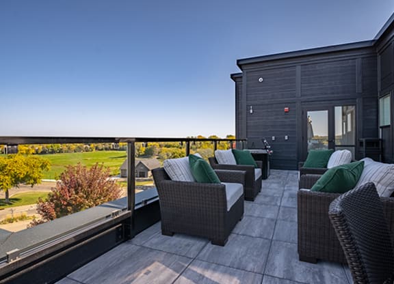 a rooftop deck with wicker furniture and a view of a golf course