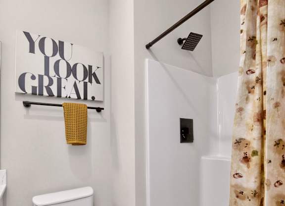 A white toilet sits under a You Look Great sign in a small bathroom.