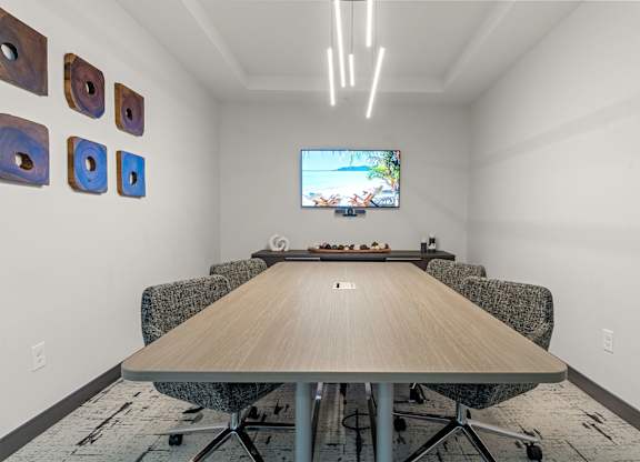 A conference room with a long table and chairs, a television on the wall, and decorative pieces on the wall.