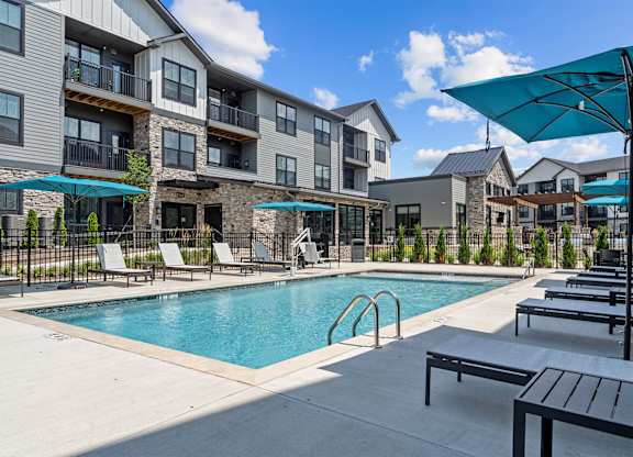 A swimming pool surrounded by lounge chairs and umbrellas in front of apartment buildings.