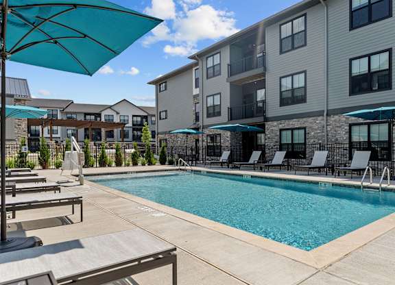 A swimming pool surrounded by lounge chairs and umbrellas in front of apartment buildings.