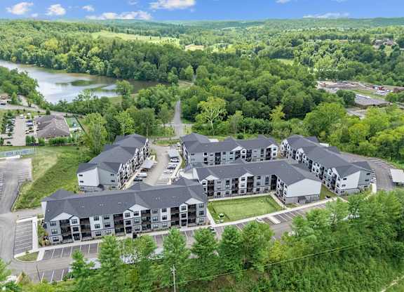 A large apartment complex is surrounded by trees and a body of water.