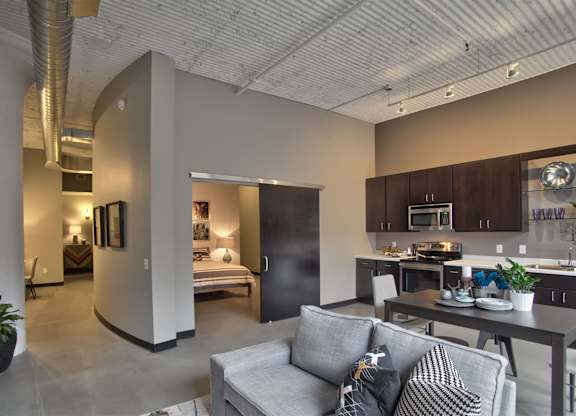 A modern living room with a grey couch and a kitchen area in the background.