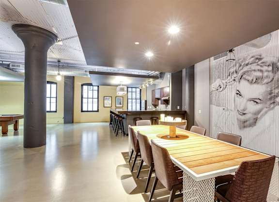 A long wooden table is surrounded by chairs in a room with a large poster on the wall.