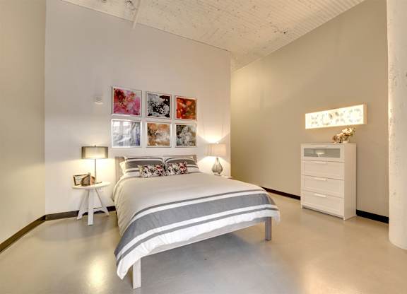 A bedroom with a bed, nightstand, and a white dresser.