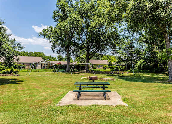A green picnic table sits in the middle of a grassy field.